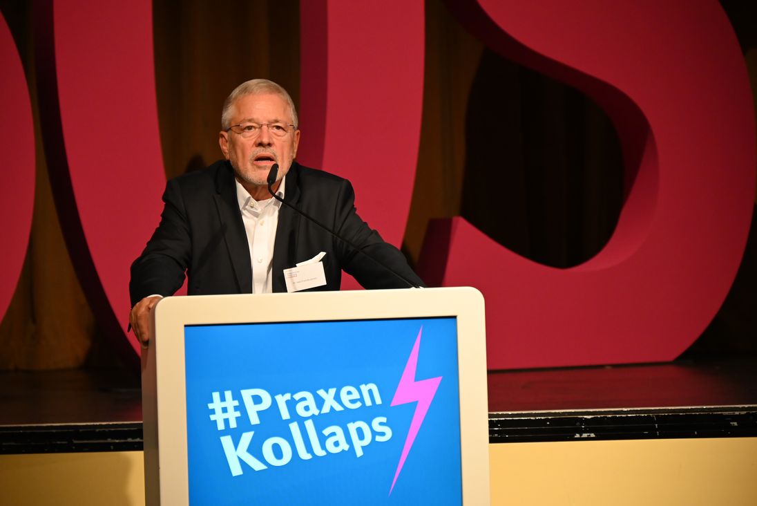Das Bild zeigt Dr. Frank Bergmann während einer Rede auf der KBV VV. Am Podium ist der Schriftzu #Praxenkollaps.